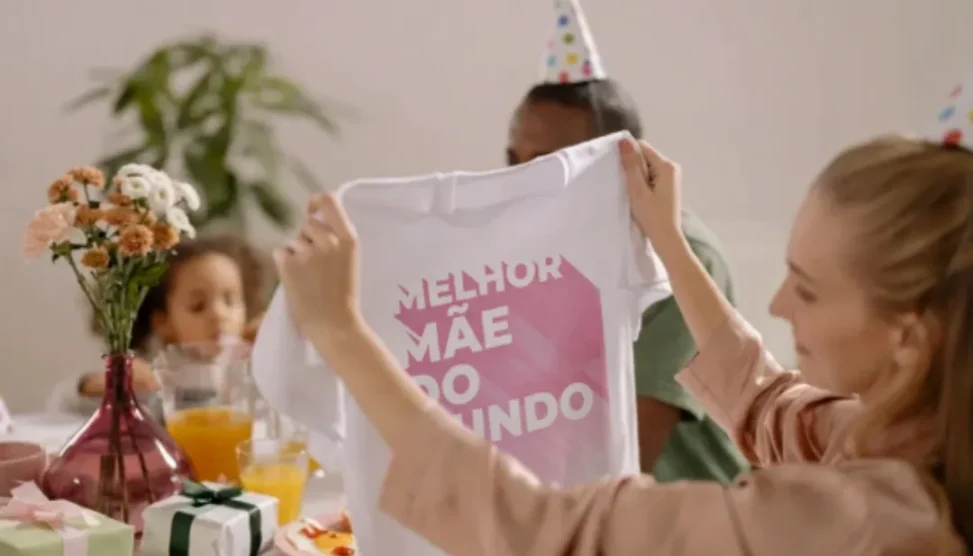 Mãe e filha sorrindo e se abraçando em um dia ensolarado, com balões de festa ao fundo