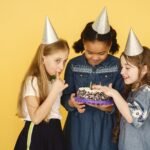 Duas amigas rindo e abraçando em uma festa de aniversário, com balões coloridos ao fundo.