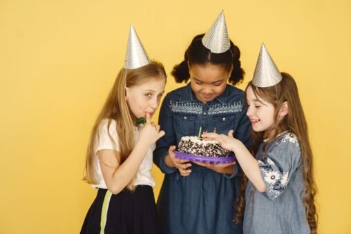 Duas amigas rindo e abraçando em uma festa de aniversário, com balões coloridos ao fundo.