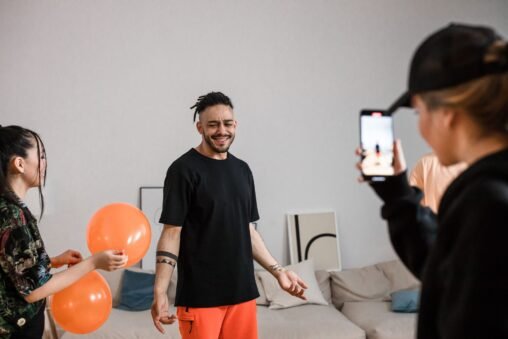 Duas amigas rindo e celebrando um aniversário com balões e confetes, tirando uma selfie para redes sociais.