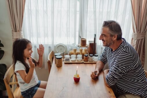 Mãe e pai sorrindo abraçando a filha em uma festa de aniversário com balões e bolo