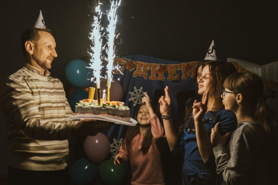 Pai ou mãe abraçando a filha em seu aniversário, com balões e um celular exibindo um status do WhatsApp