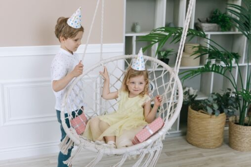 Dois irmãos rindo e se abraçando em um sofá, com balões de aniversário ao fundo, transmitindo carinho e diversão.